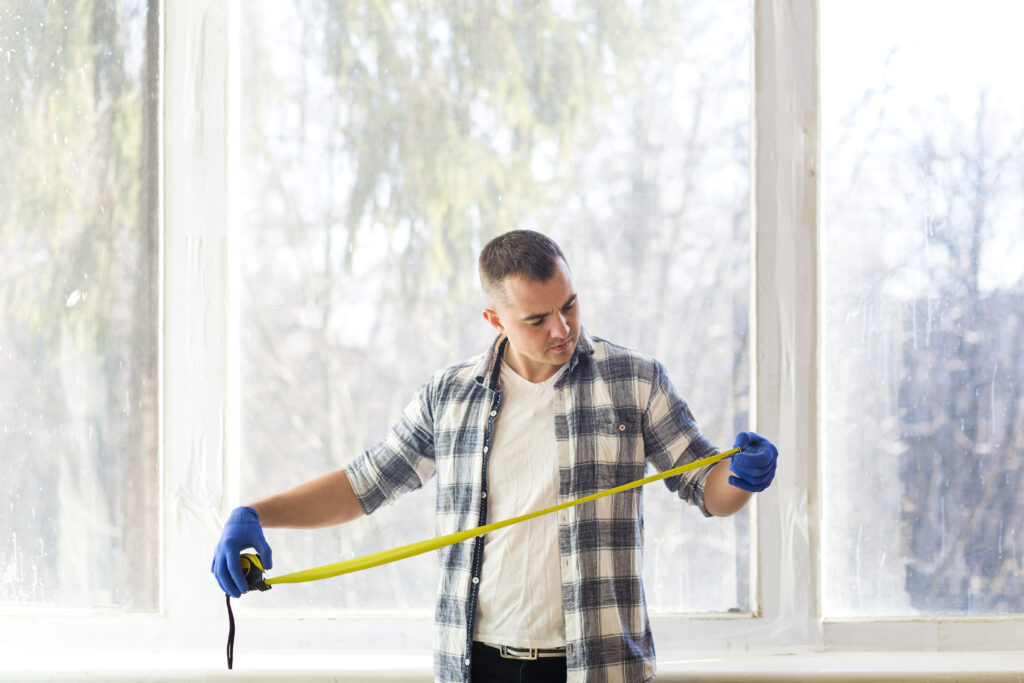 Man looking at measuring tape in front of windows